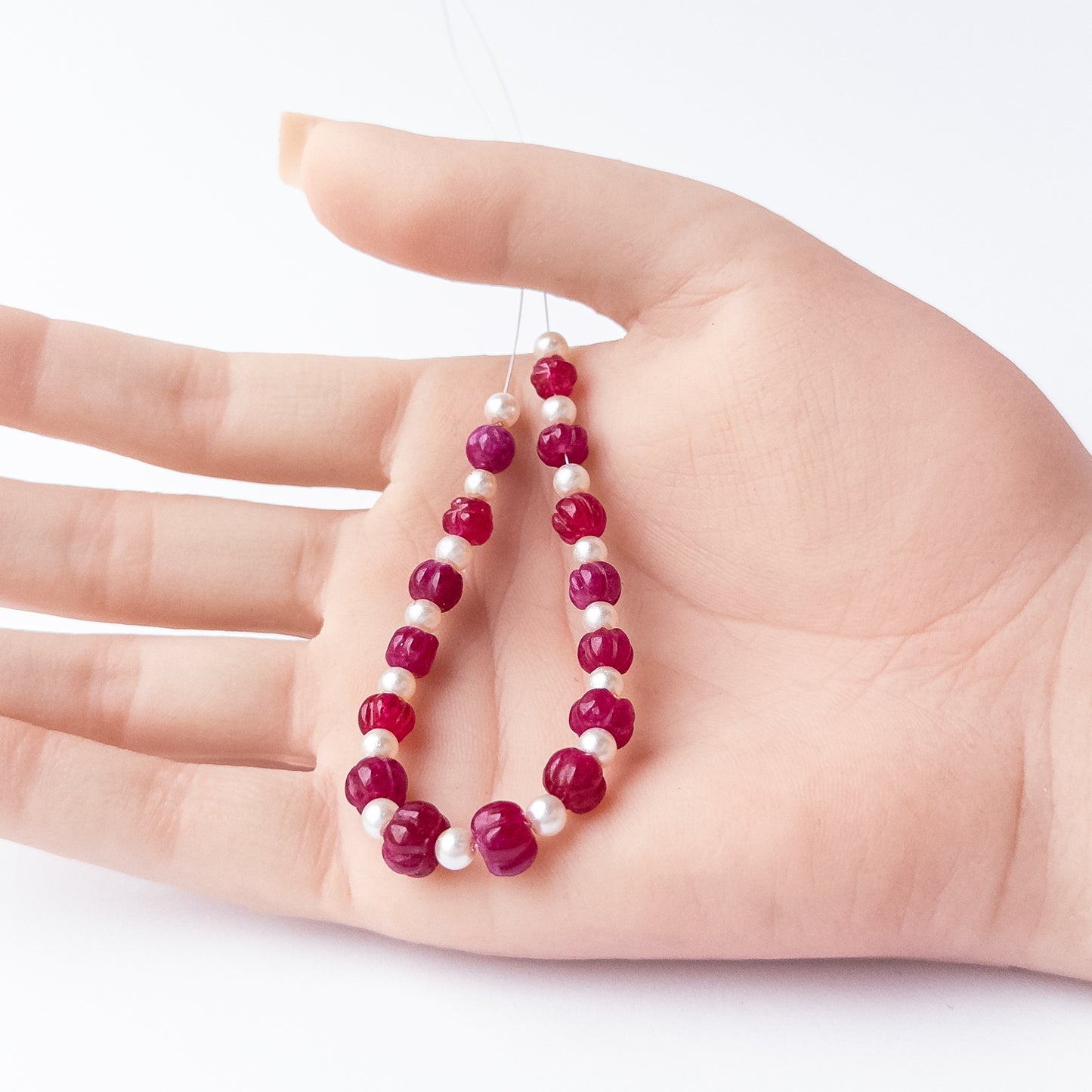 A person holds delicate strands of Quartz and Shell Pearl beads, showcasing their pumpkin‑cut design.