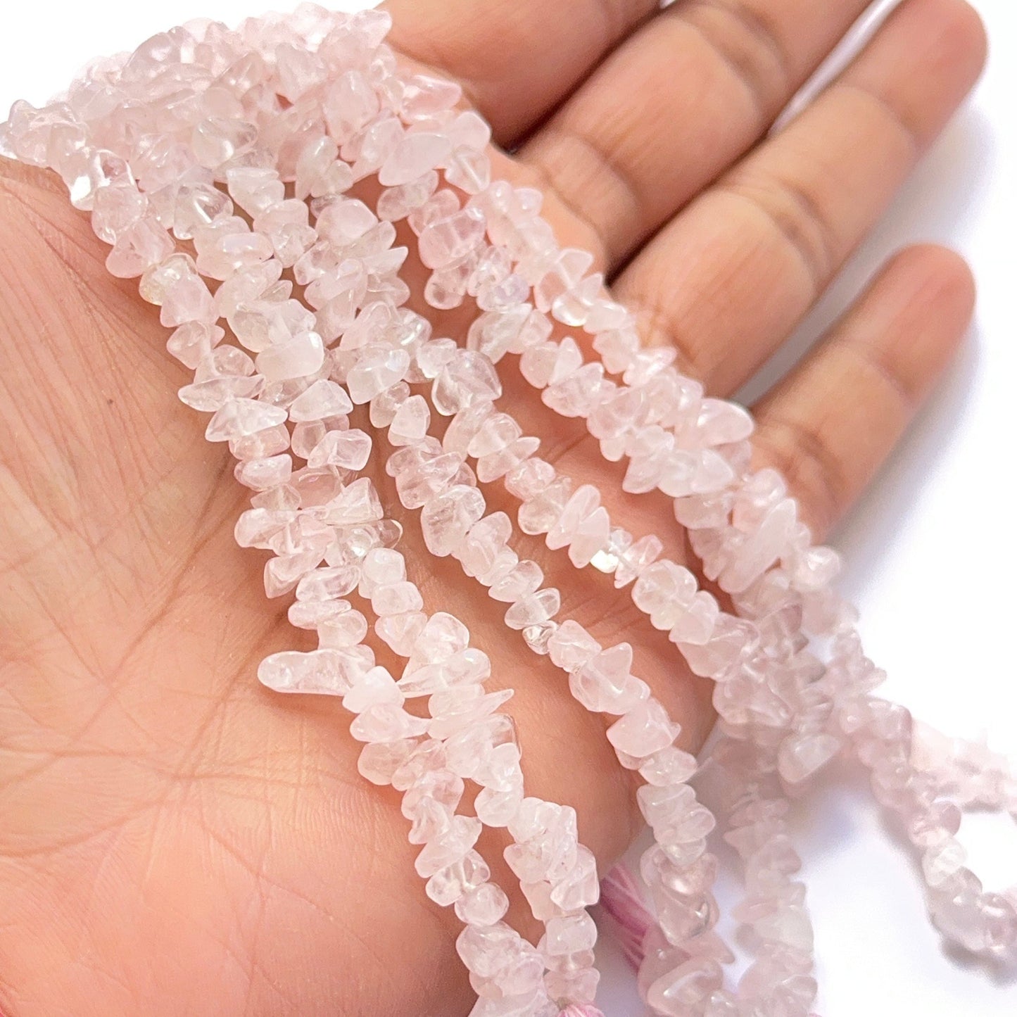 A person holds delicate strands of rose quartz beads, showcasing their smooth design