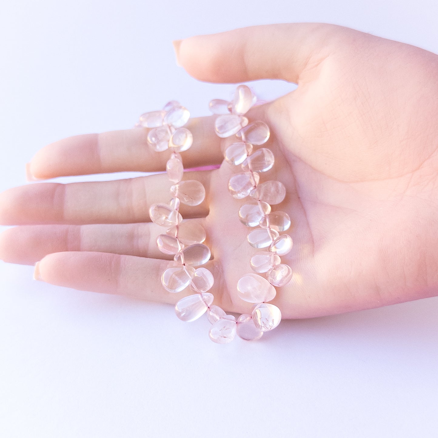 A person holds delicate strands of Rose Quartz beads, showcasing their smooth briolette design.
