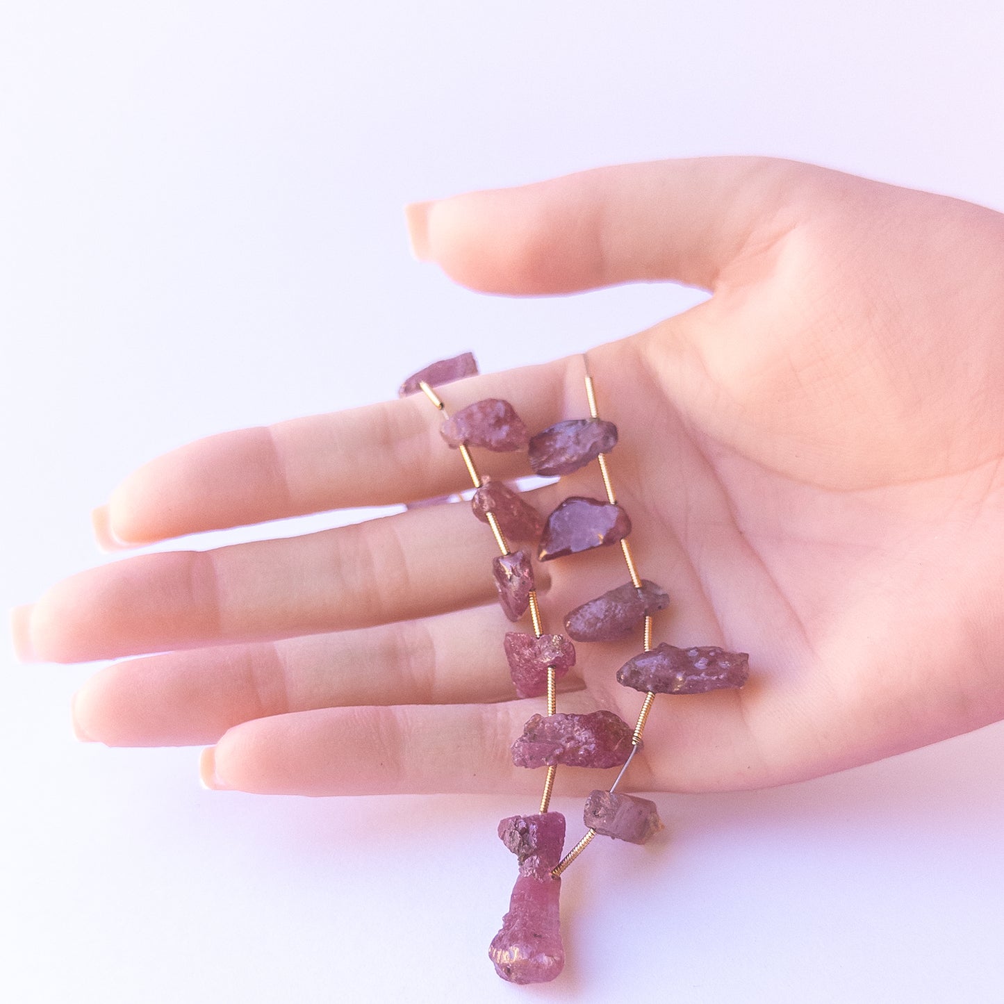 A person holds delicate pieces of Ruby rough beads, showcasing their drilled rough design.