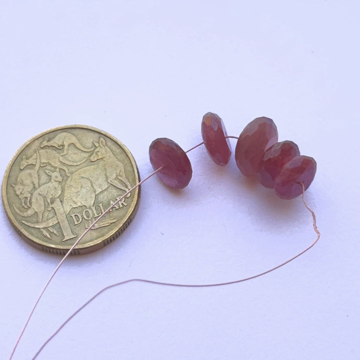 Ruby gemstone beads , highlighting cut, clarity and arrangement and placed next to a coin.