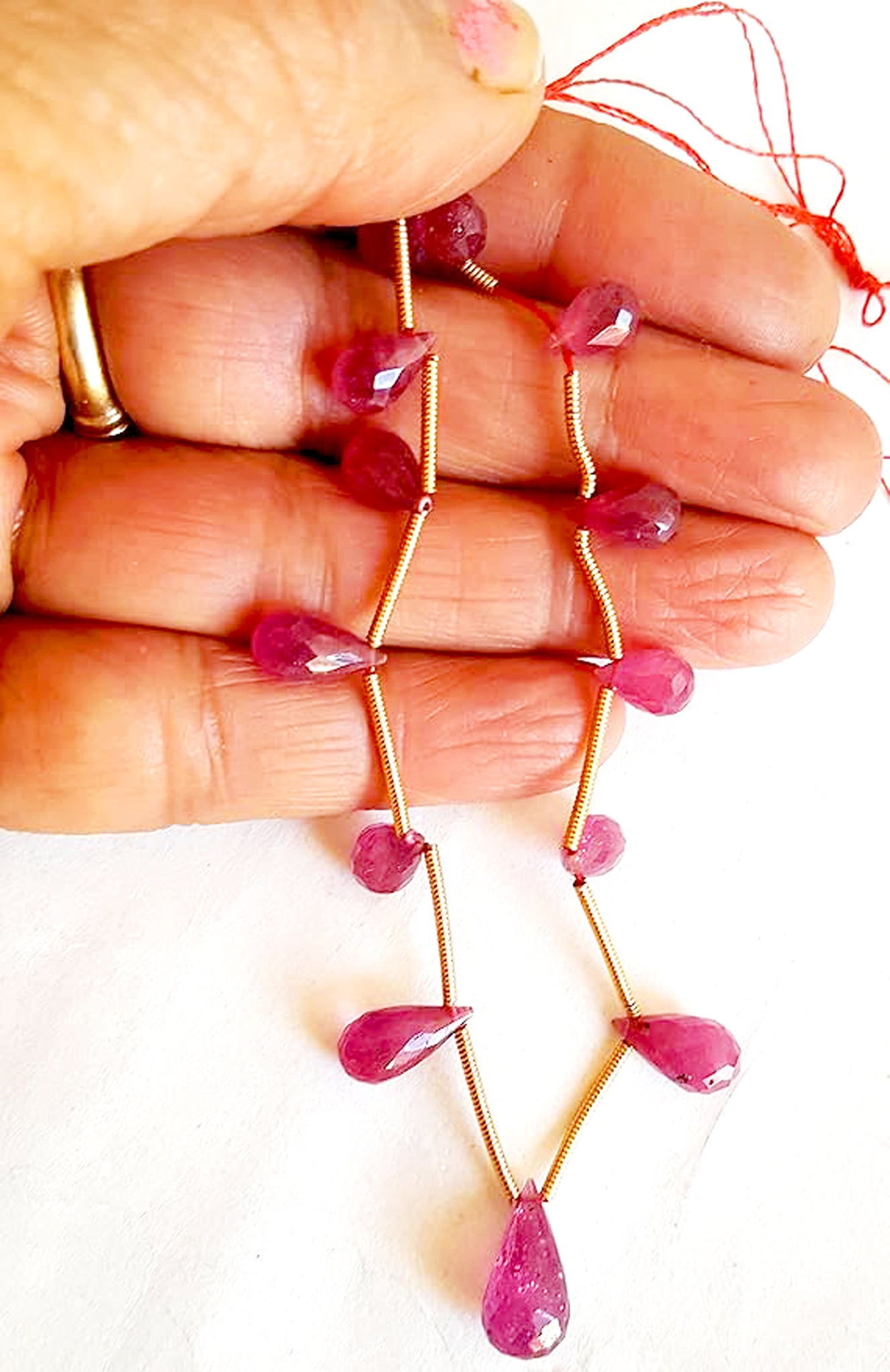 A person holds delicate strands of ruby beads, showcasing their smooth design.