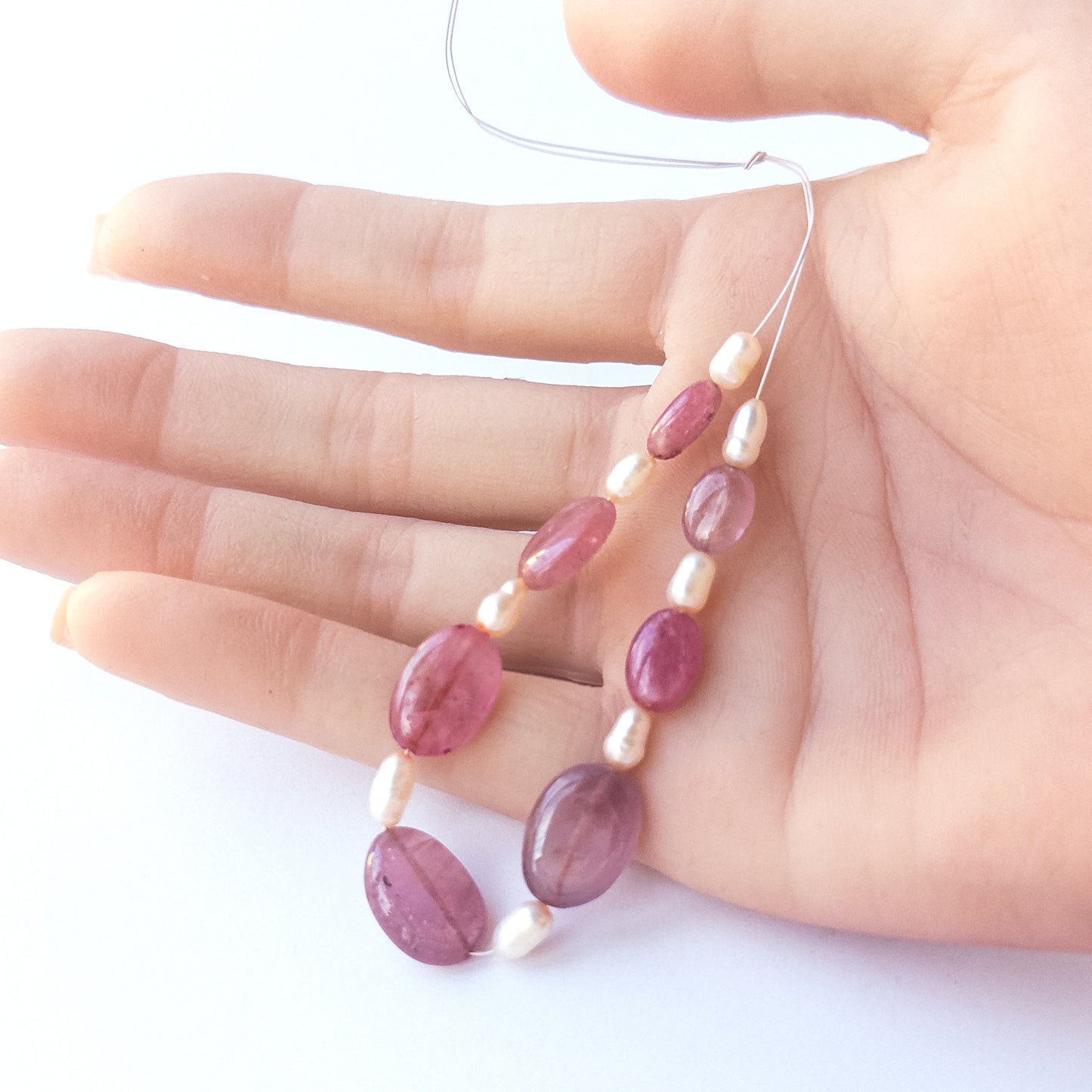 A person holds Ruby and pearl beads, showcasing their size variation and natural shine.