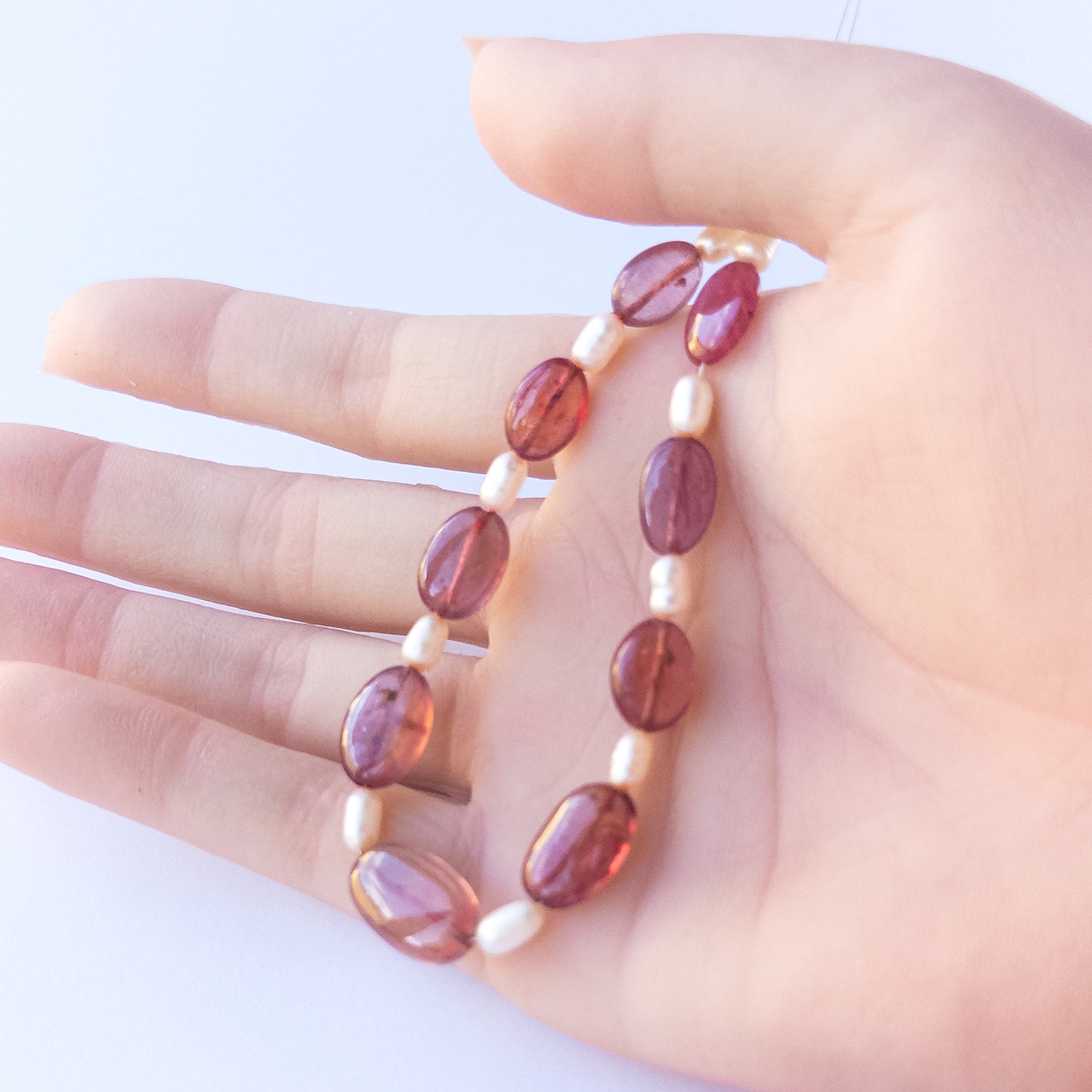 A person holds Ruby and pearl beads, showcasing their size variation and natural shine.