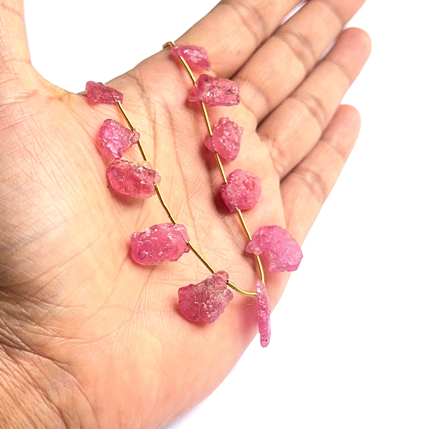 A person holds delicate strands of ruby rough beads, showcasing their smooth design.