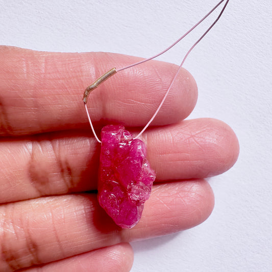 Ruby rough bead on a wire held between fingers against a white background