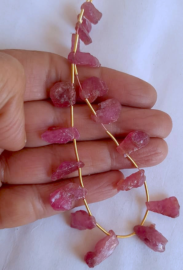 A person holds delicate strands of Ruby beads, showcasing their natural rough design.
