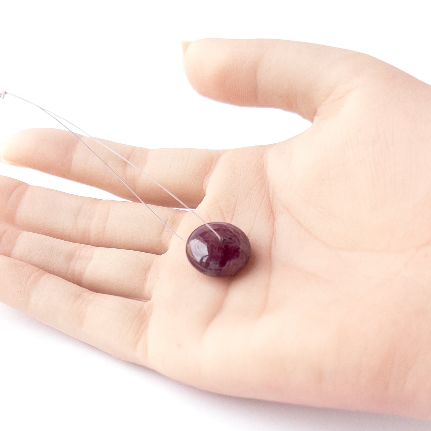 A person holds delicate pieces of Ruby beads, showcasing their smooth disc design.
