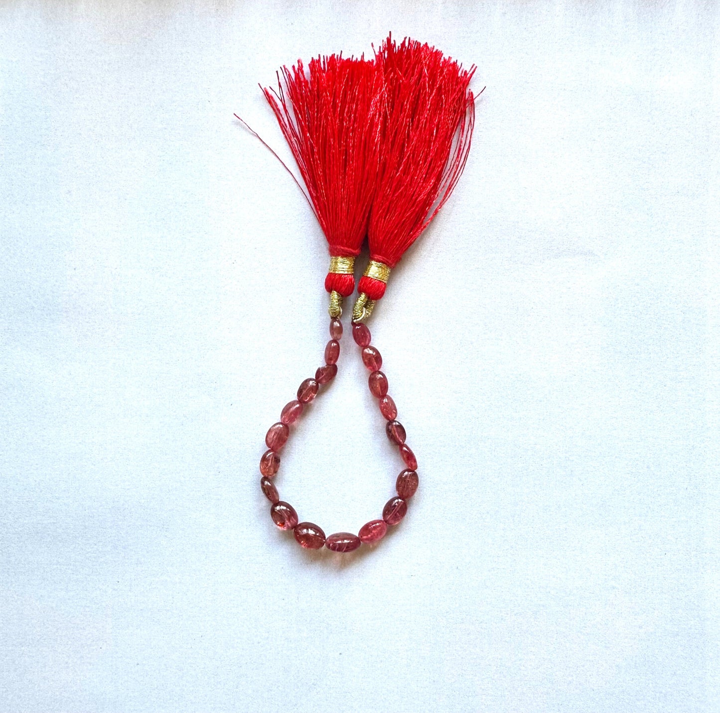 Ruby bead strand featuring smooth oval cut and deep red colour, arranged in graded sizes.