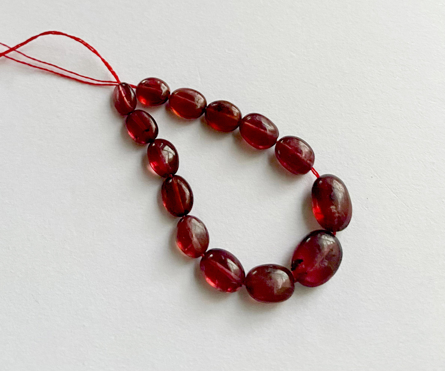 Strand of 24-carat ruby beads with glossy surface and consistent oval shape.