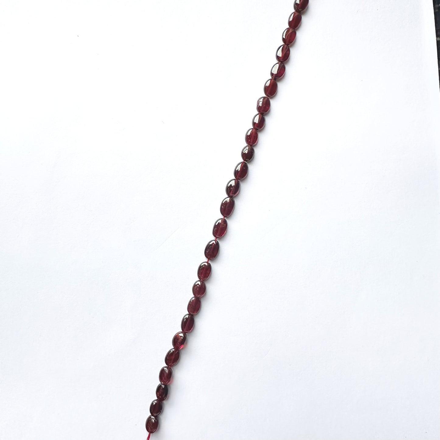 Close-up of Ruby beads arranged in a 20cm strand with glossy surface and rich hue.