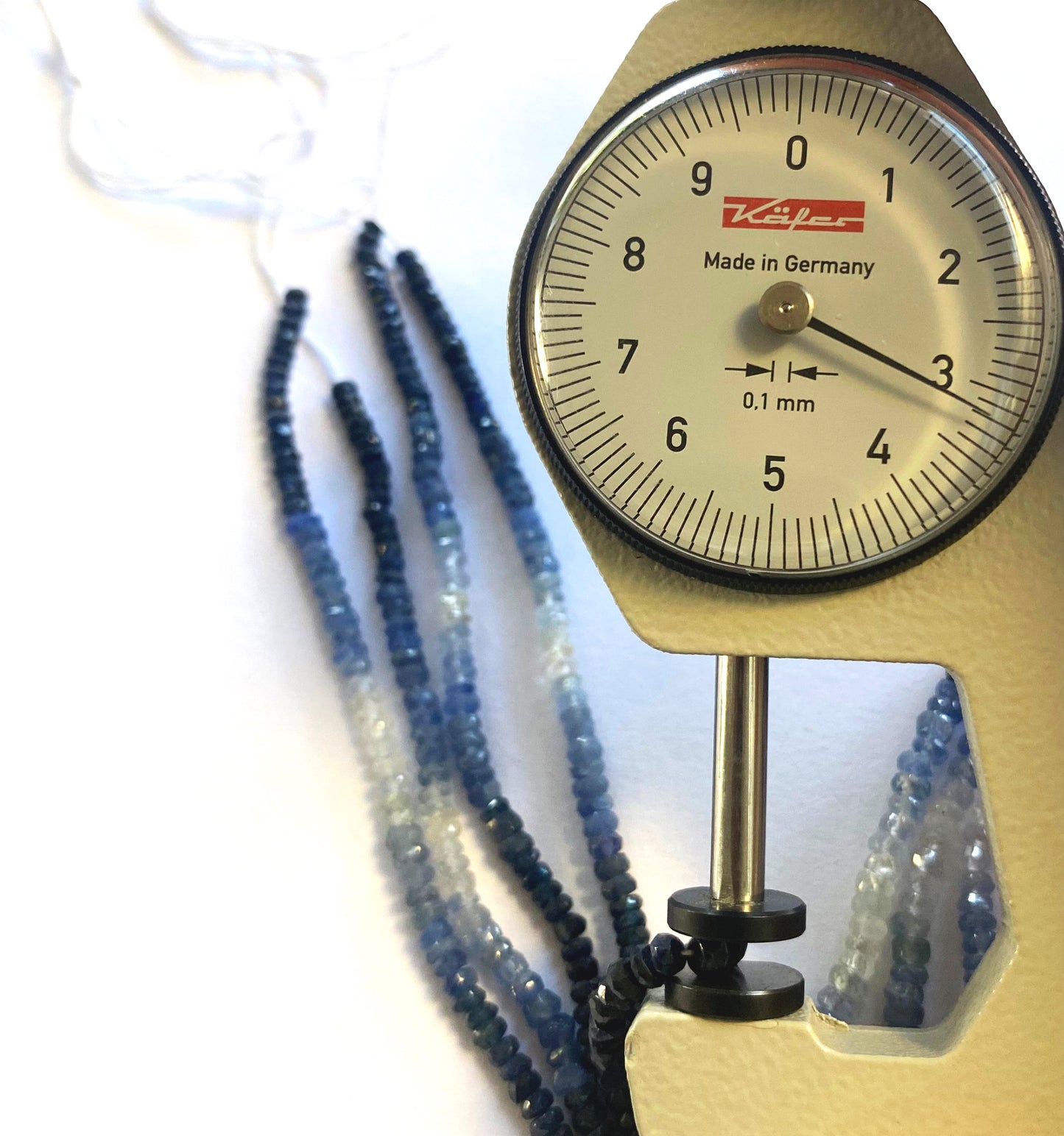 A dial gauge measures the Blue Sapphire faceted rondelle 2.8–3.5mm gemstone for sizing precision.