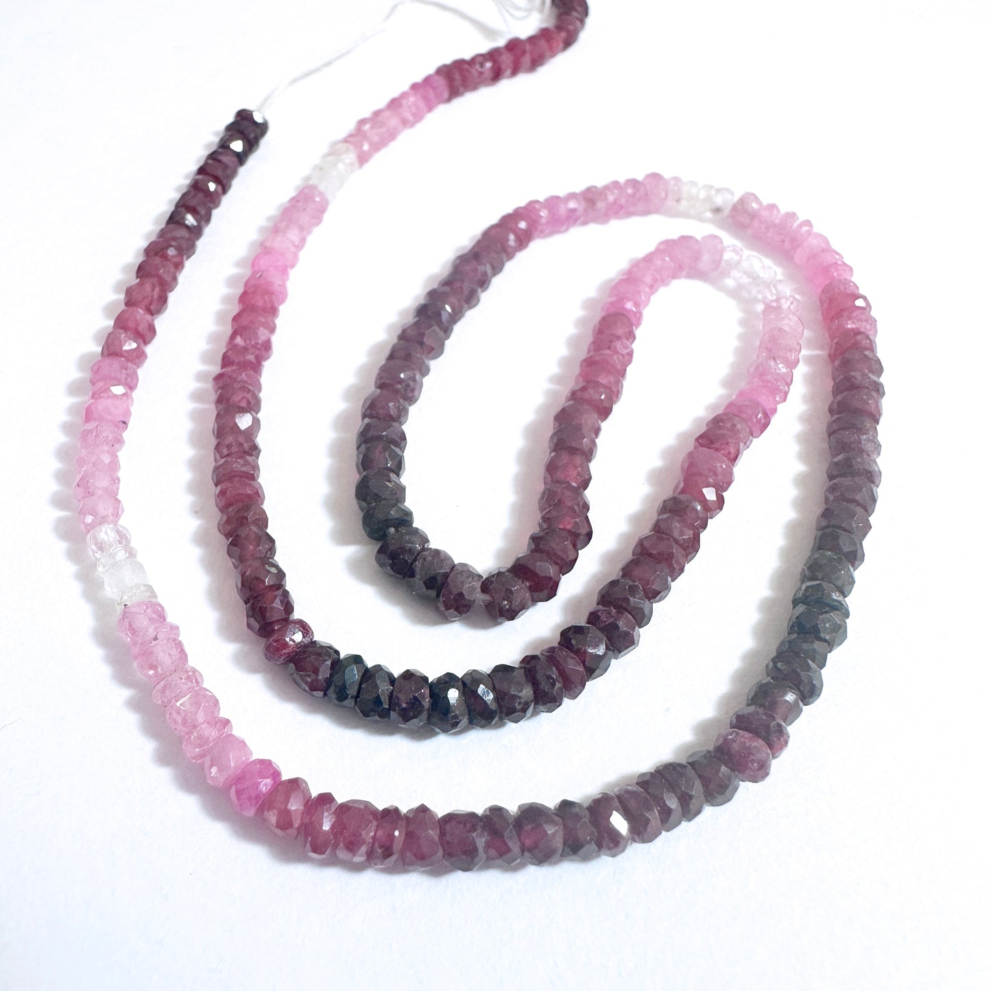 Ruby gemstone beads with faceted rondelle shape reflect light beautifully on a white background.