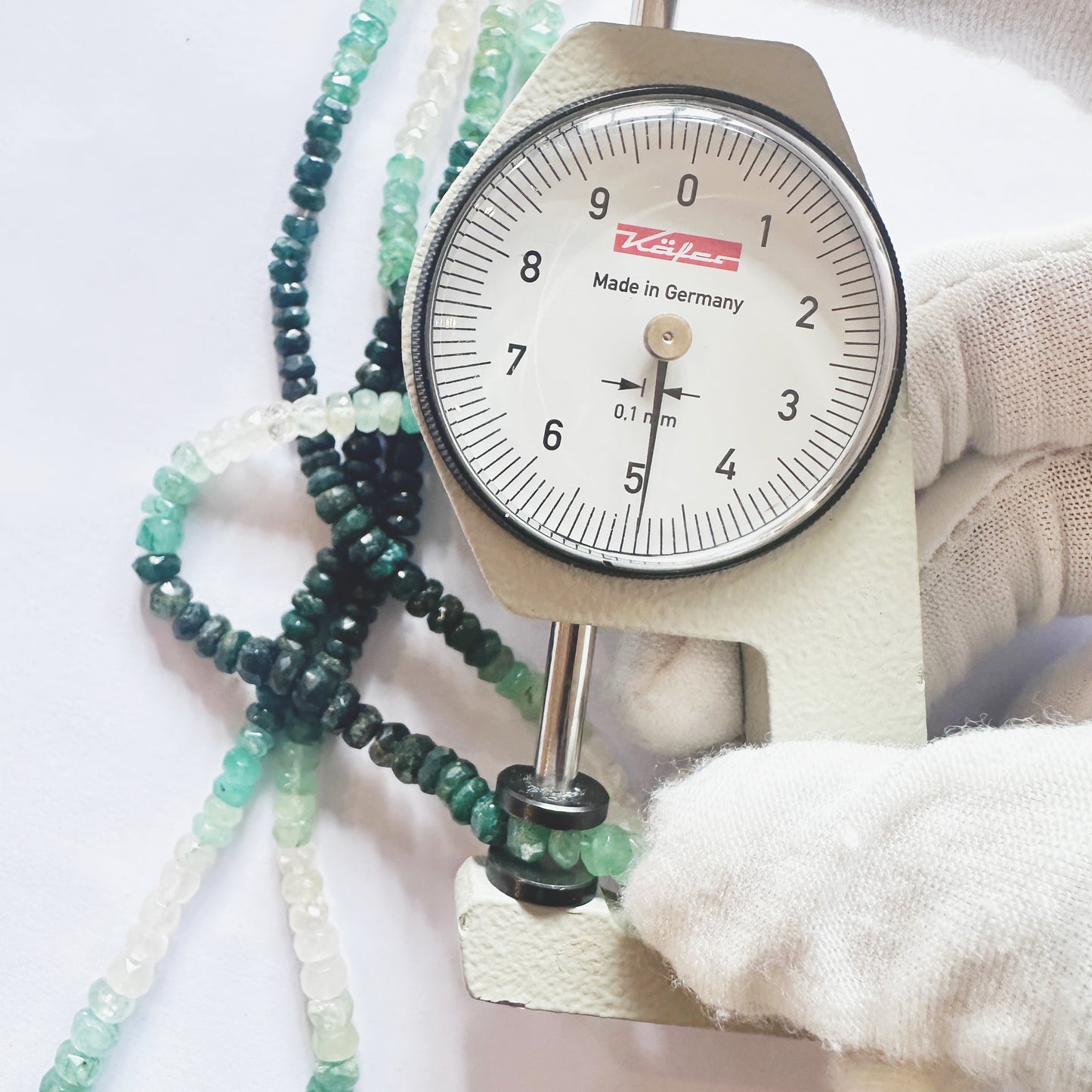 A dial gauge measures the Emerald faceted rondelle 3.6-5mmmm gemstone.