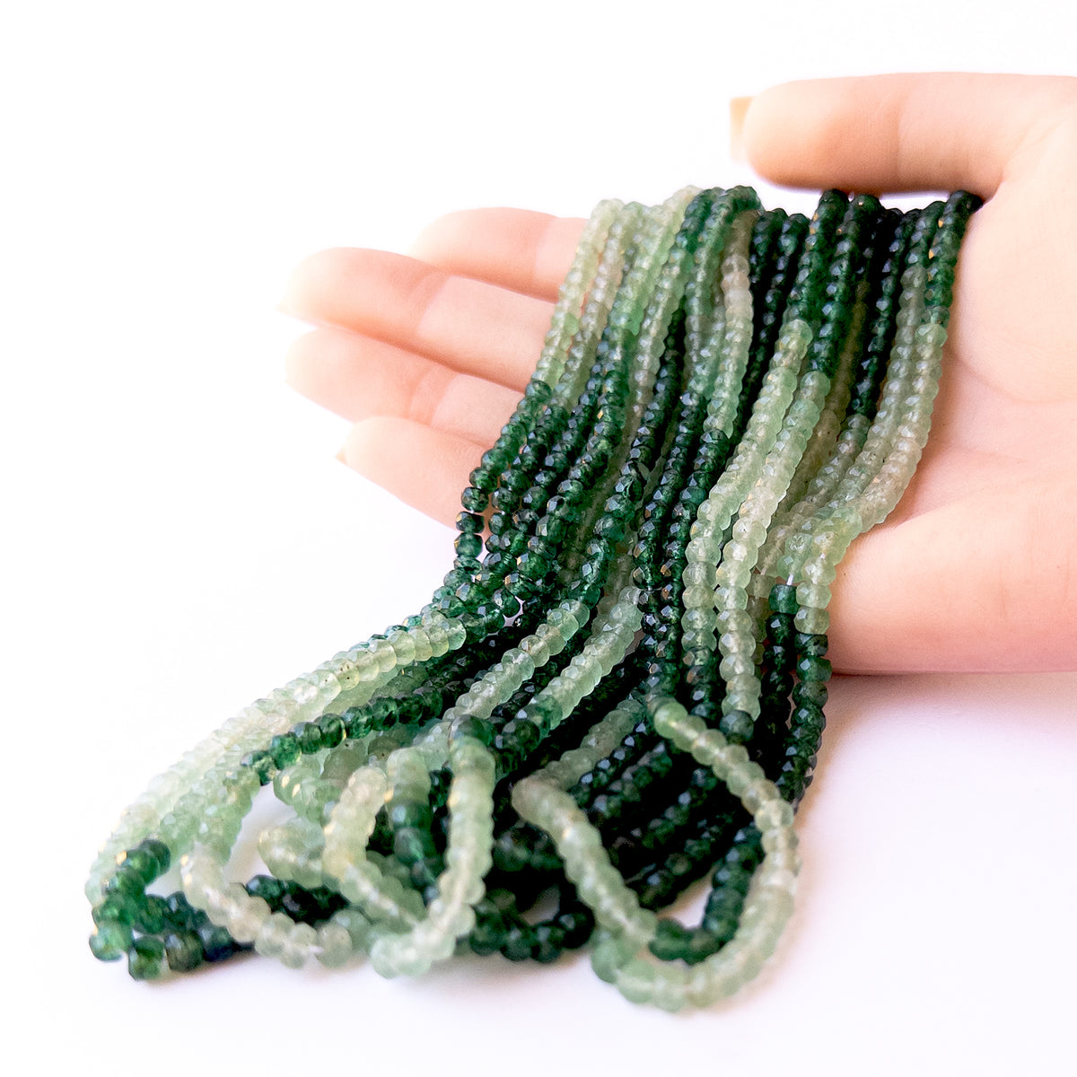 A person holds delicate strands of Shaded Green Quartz beads, showcasing their faceted rondelle design.