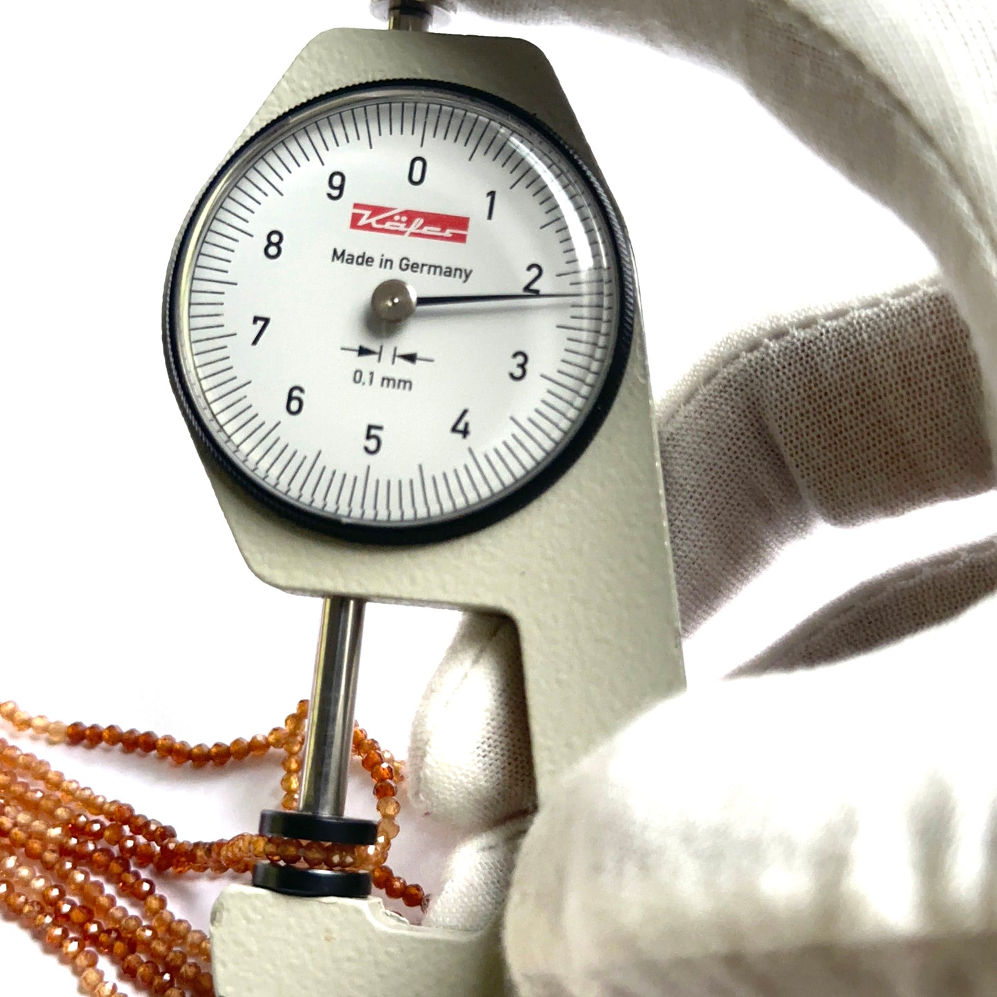 A dial gauge measures the shaded hessonite faceted rondelle 2.2mm gemstone.