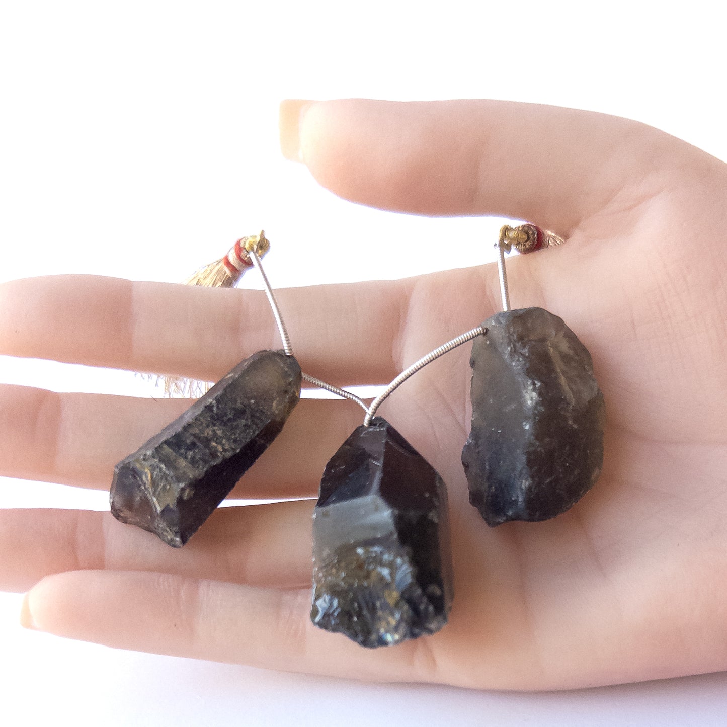 A person holds delicate pieces of Smoky Quartz rough beads, showcasing their drilled rough design.