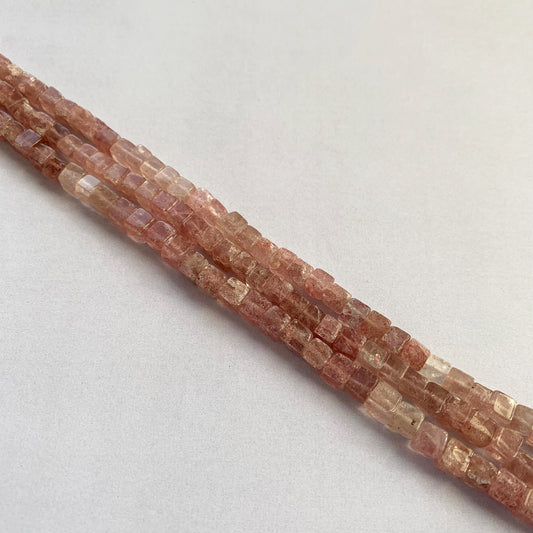 Arrangement of Strawberry Quartz beads in a cube cut, highlighting their translucent glow and pastel tones.
