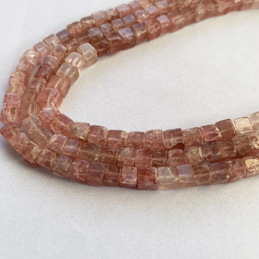 Close-up view of polished 4.4-4.8mm Strawberry Quartz cube beads showcasing subtle shimmer and clarity.