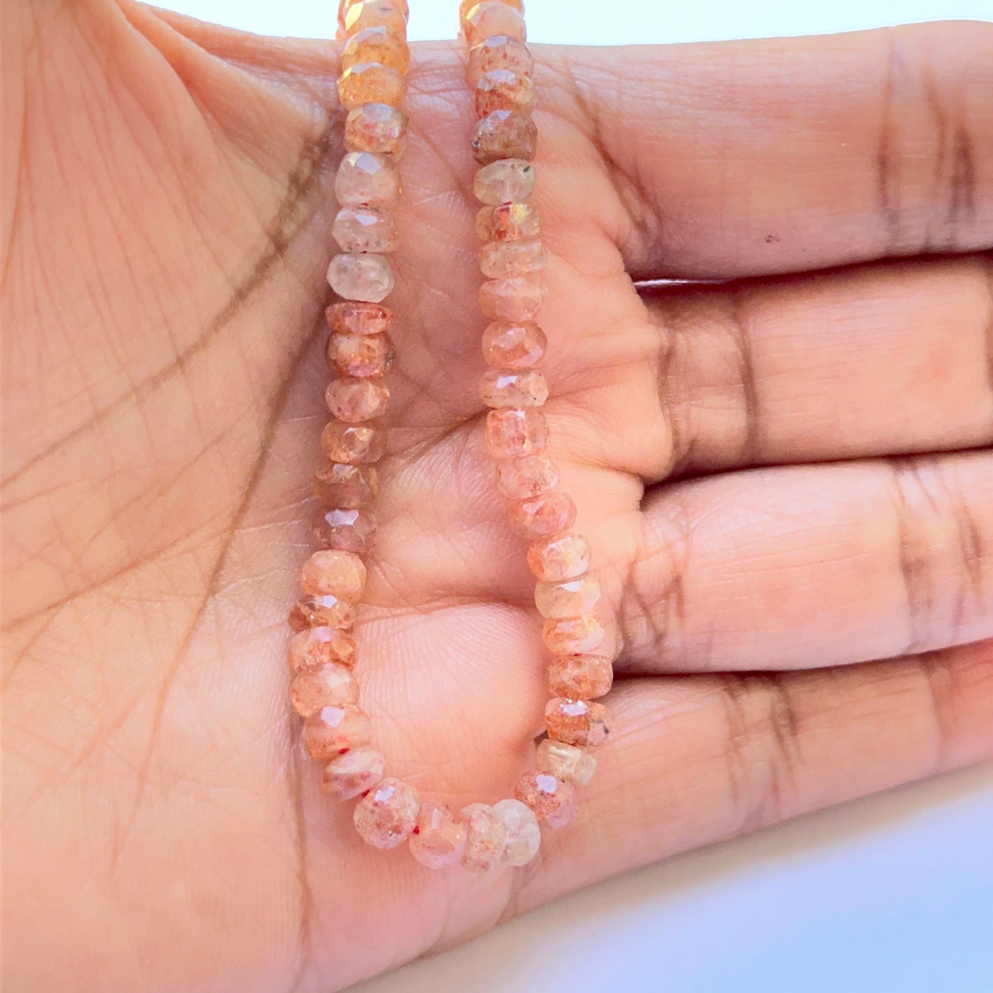 A person holds delicate strands of Sunstone beads, showcasing their smooth design.