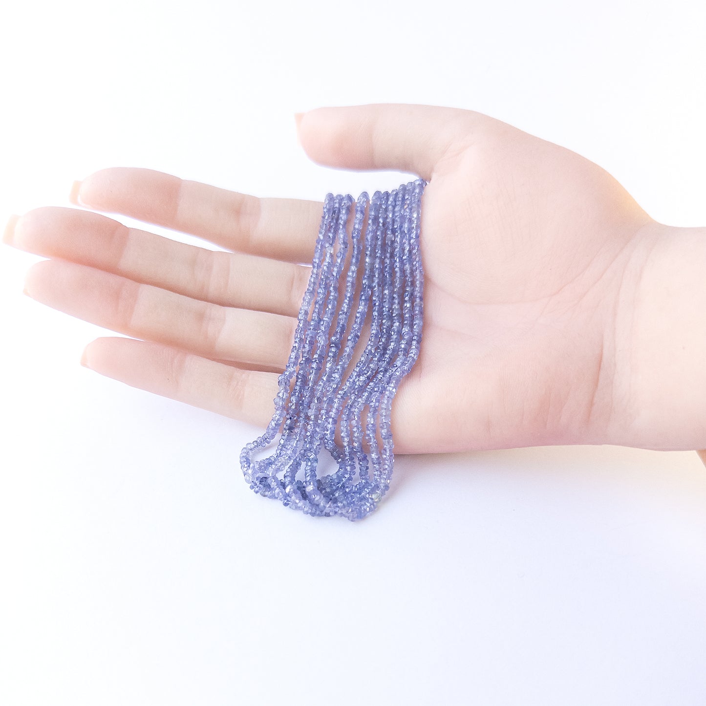 A person holds delicate strands of Tanzanite beads, showcasing their faceted rondelle design.