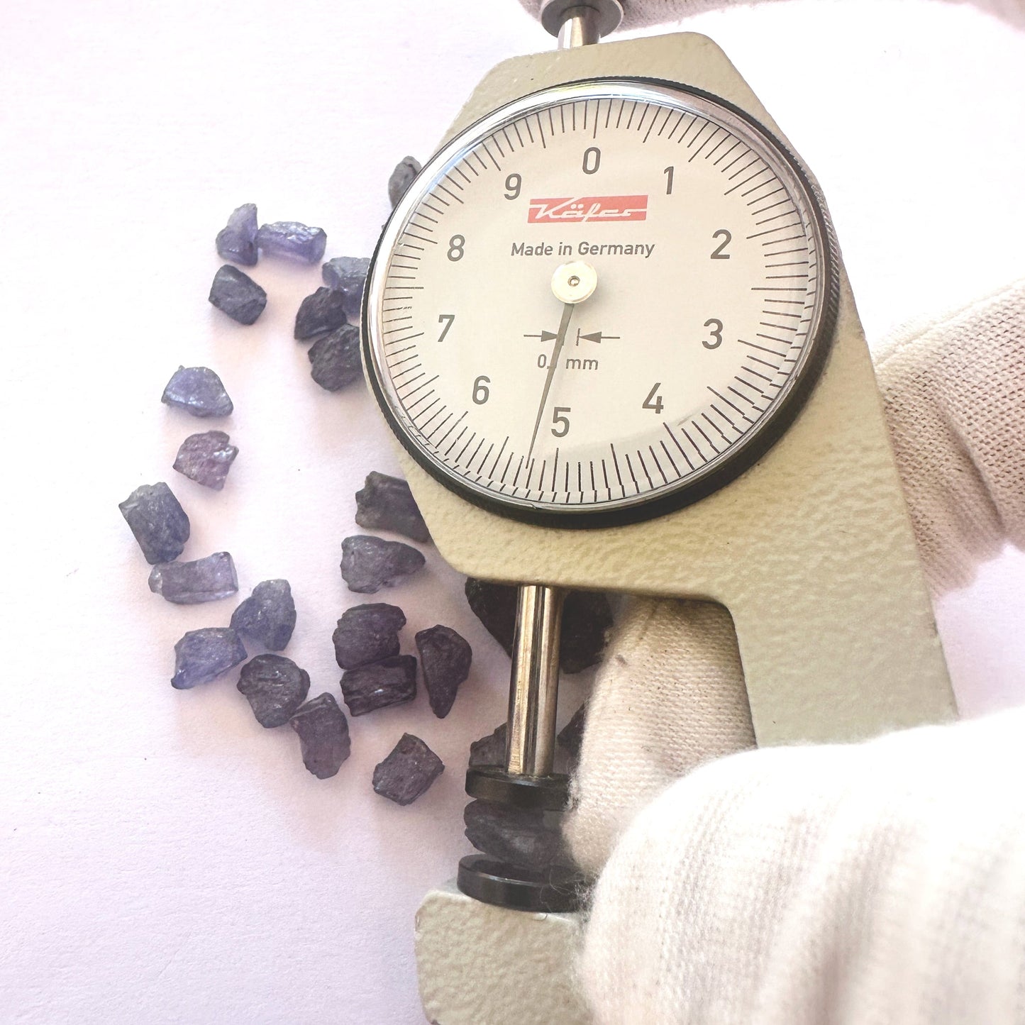A dial gauge measures the Tanzanite rough cut 5-6mm gemstone.