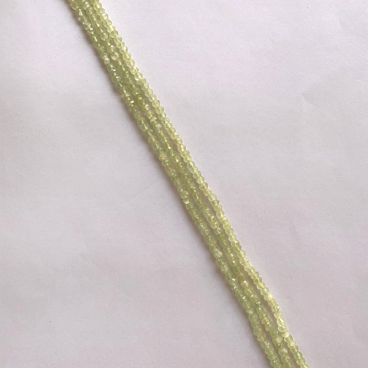 A strand of faceted Prehnite rondelle beads in soft green tones, arranged neatly on a 33cm string.
