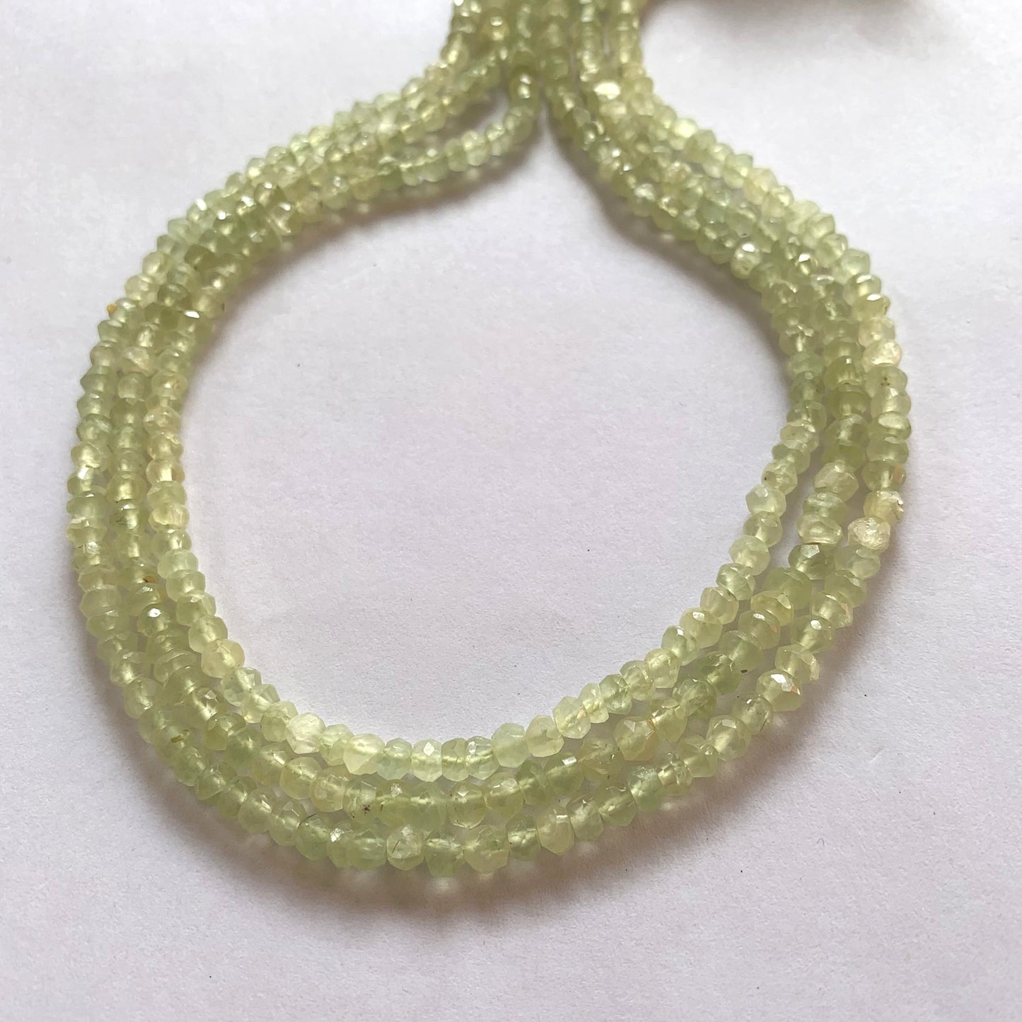 Prehnite gemstone beads strung in a continuous loop, reflecting light from their faceted surfaces.