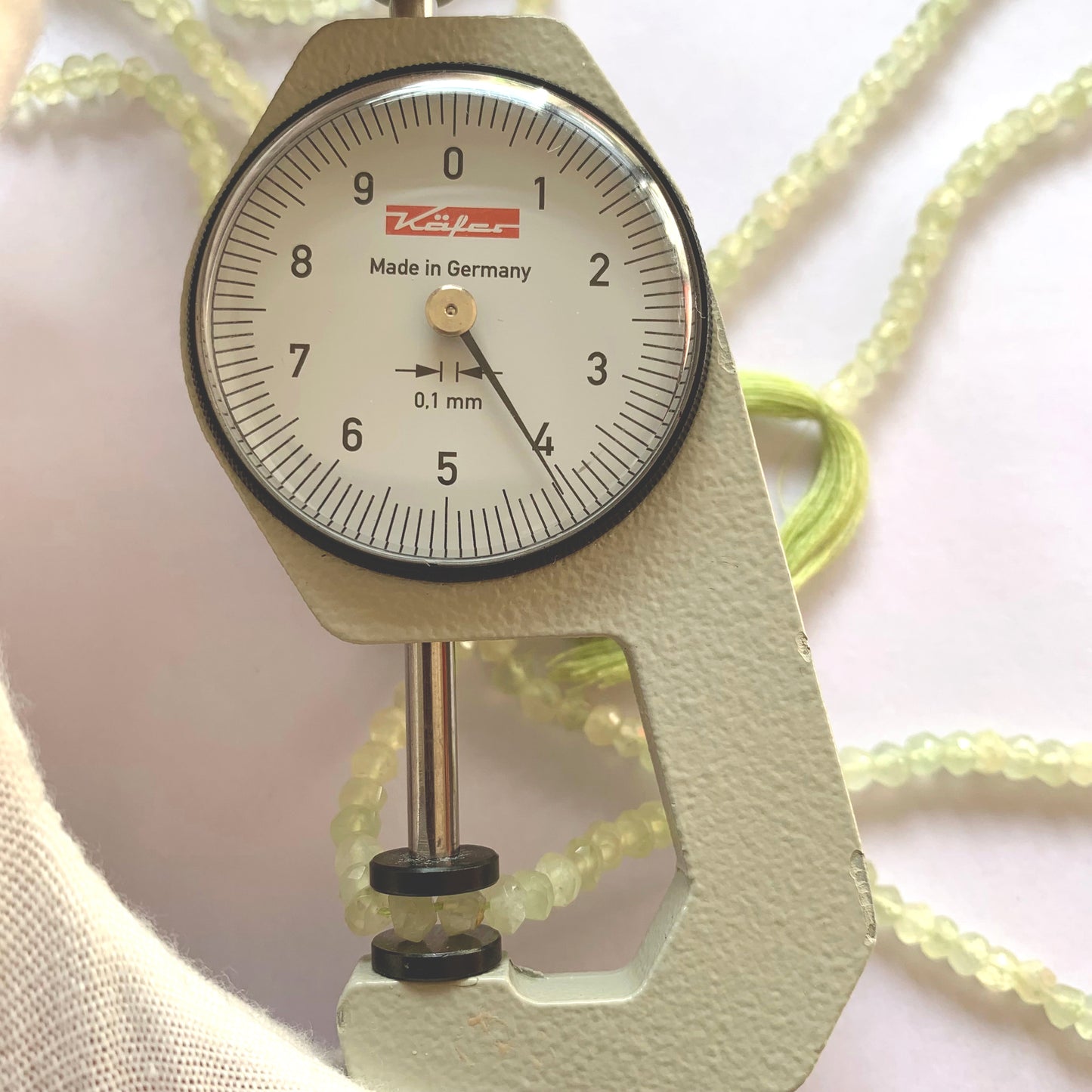 A dial gauge measures the Prehnite faceted rondelle 4.0–4.2mm gemstone.