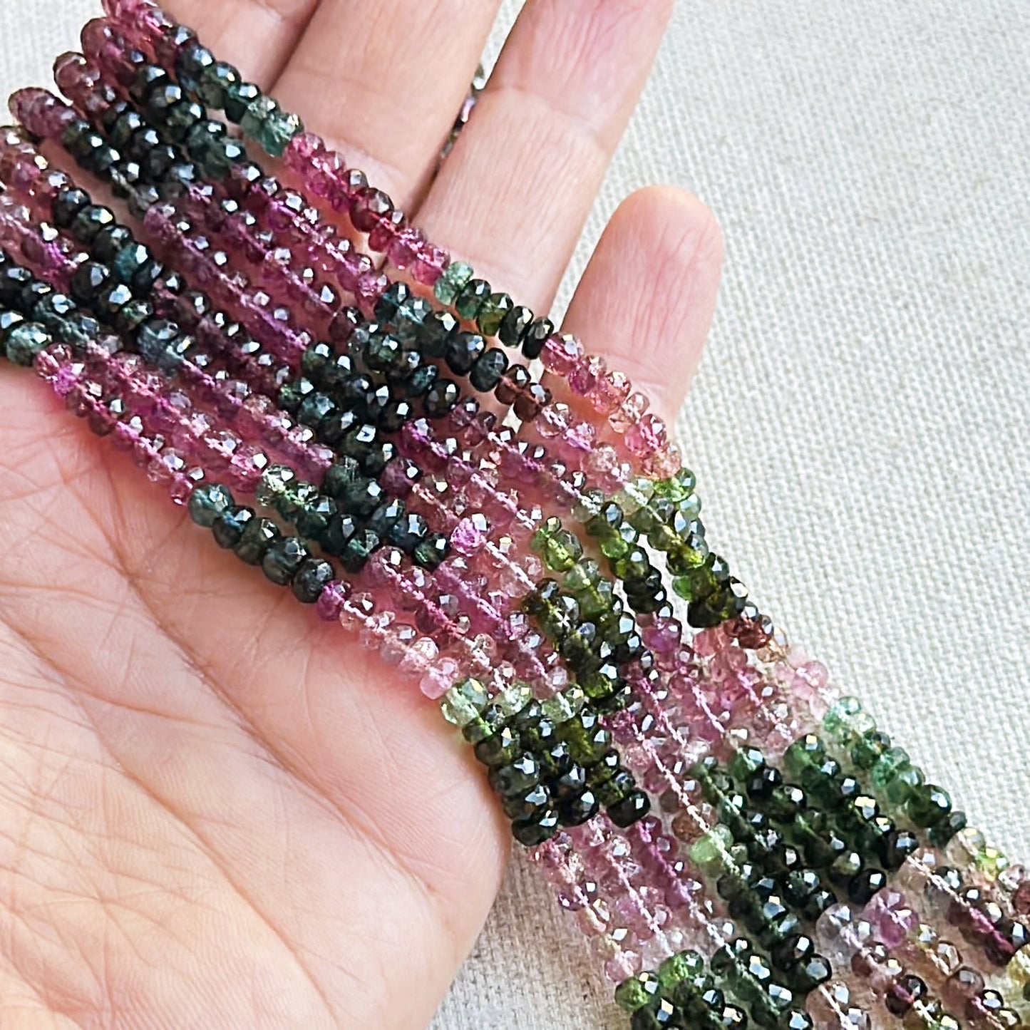 A person holds delicate strands of tourmaline beads, showcasing their faceted design.