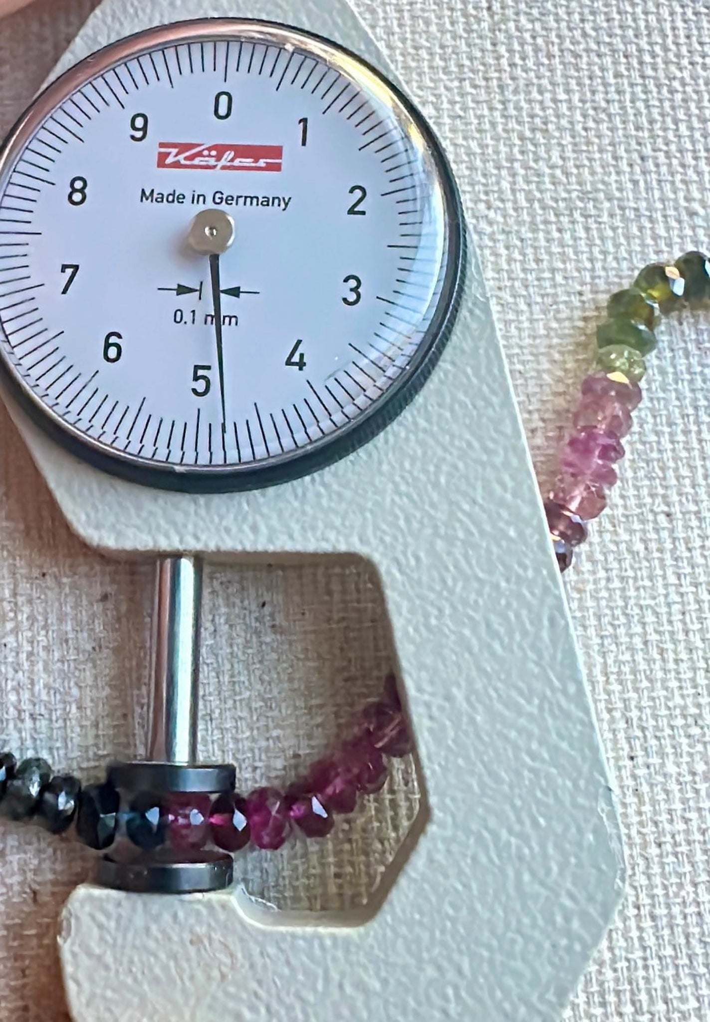 A dial gauge measures the tourmaline faceted rondelle 4.8mm–5.7mm gemstone for size accuracy.