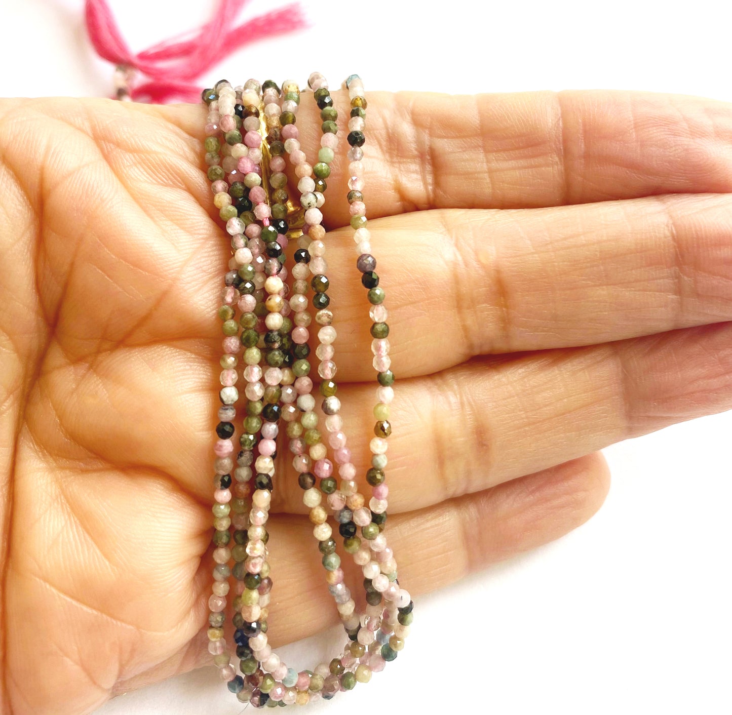 A person holds delicate strands of Tourmaline beads, showcasing their smooth design.
