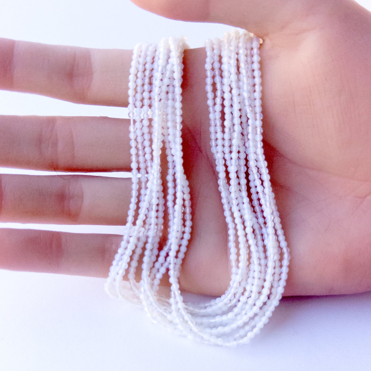 A person holds delicate strands of White Chalcedony beads, showcasing their faceted rondelle design.