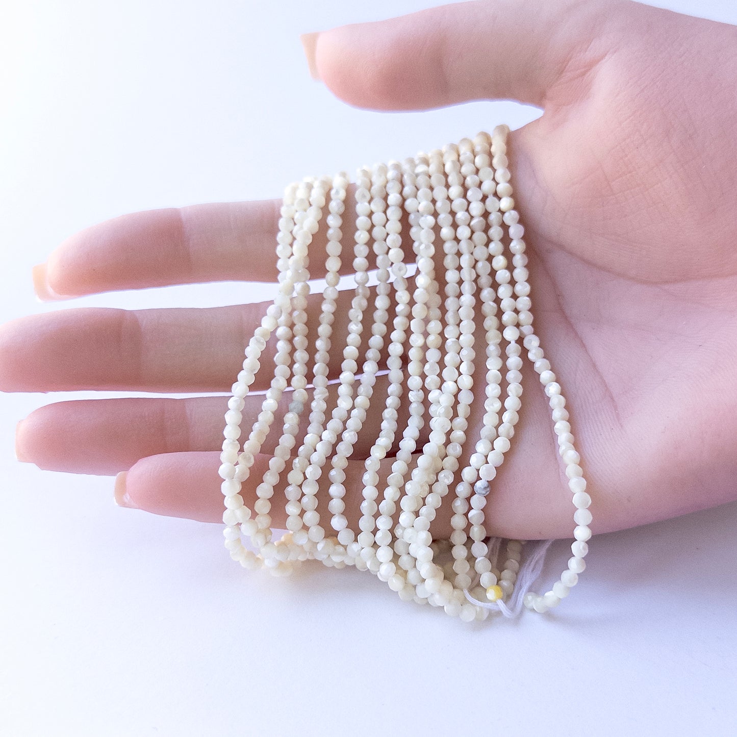 A person holds delicate strands of White Opal beads, showcasing their faceted rondelle design.