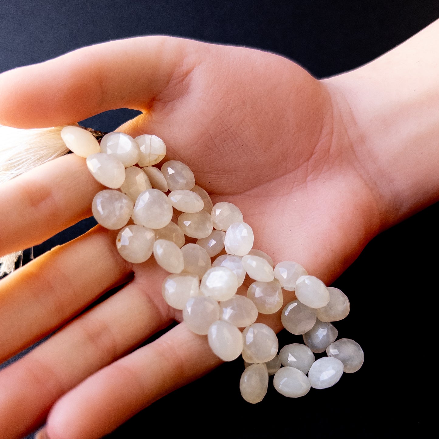 A person holds delicate strands of White Rainbow Moonstone beads, showcasing their faceted briolette design.