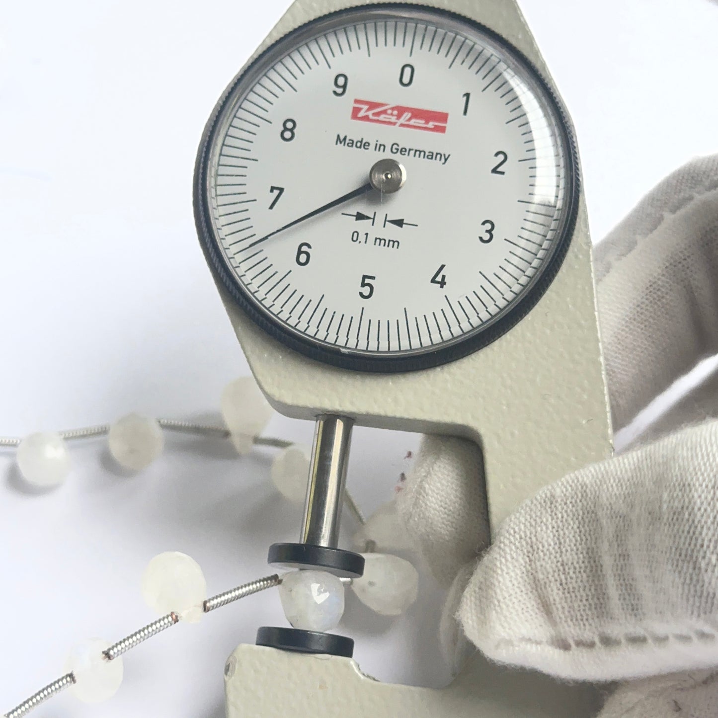 A dial gauge measures the white rainbow moonstone faceted briolette 6–7mm gemstone.