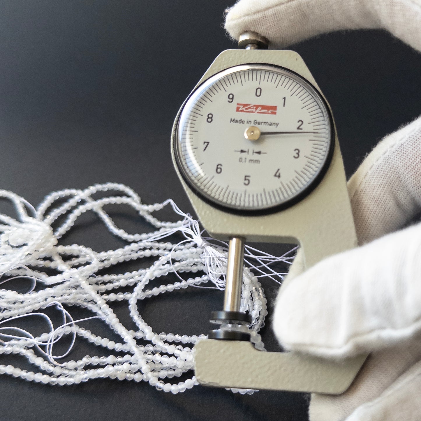 A dial gauge measures the White Rainbow Moonstone faceted rondelle 2.3–2.4mm gemstone.