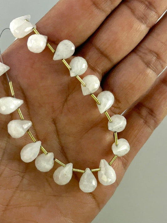 A person holds delicate strands of White Rainbow Moonstone beads, showcasing their faceted teardrop design.
