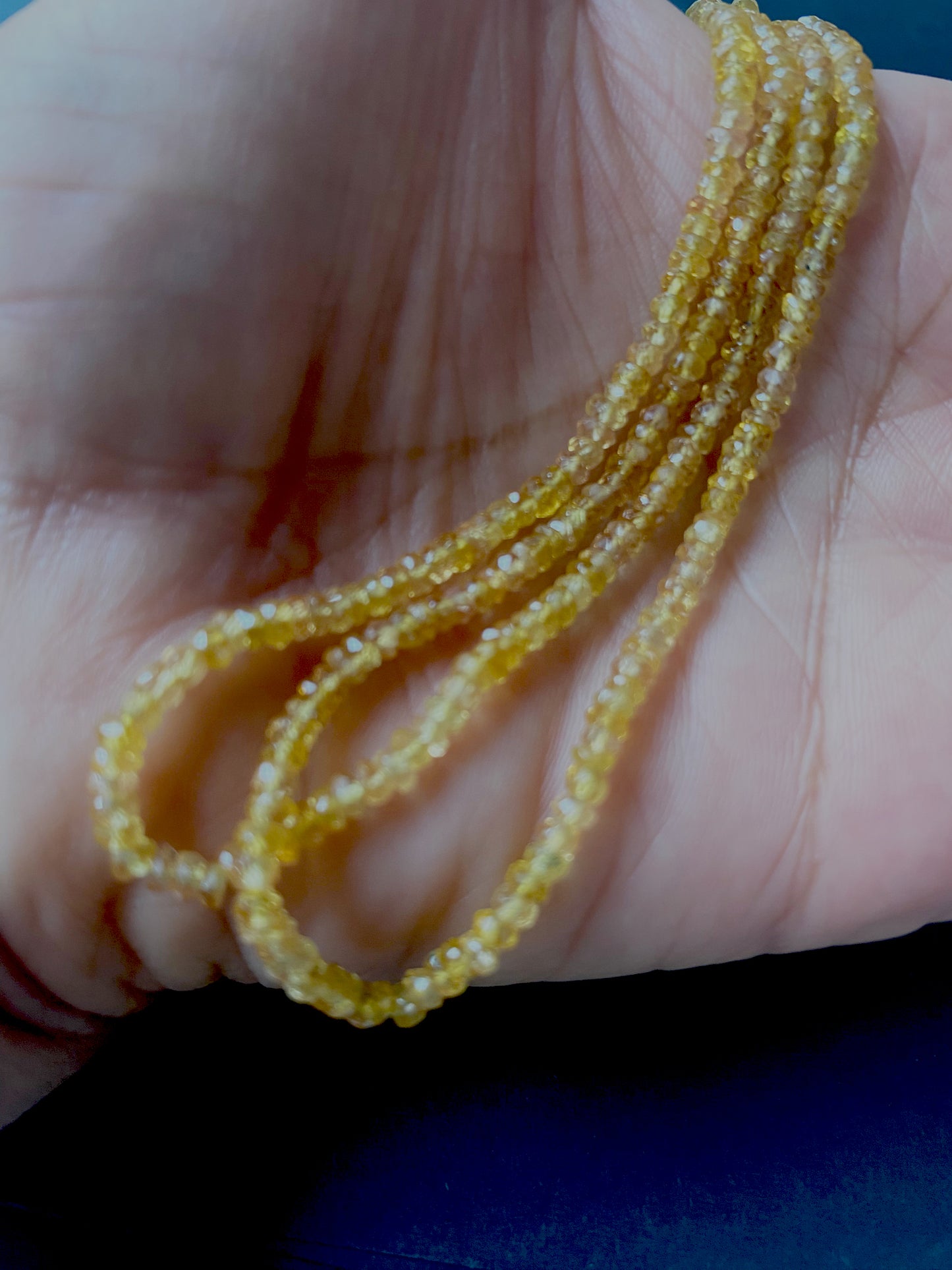 A person holds delicate strands of Yellow Sapphire beads, showcasing their colour and faceted design.