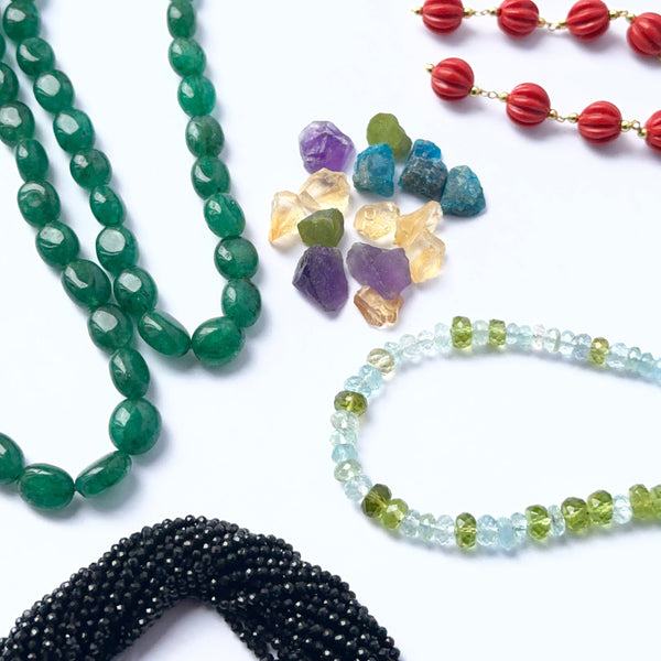 Natural gemstone variety for jewellery design: tumbled Emeralds, faceted aquamarine rondelles, round faceted corals, and raw amethyst and citrine nuggets.