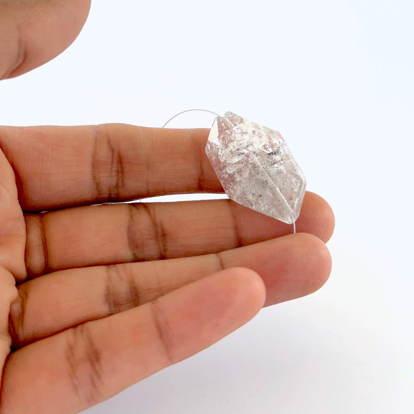 A person holds a rough Herkimer Diamond bead, showcasing its top drilled design.
