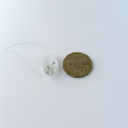 A coin is placed near a rough Herkimer Diamond bead for scale.