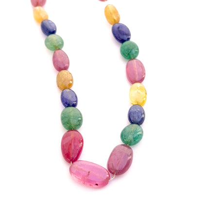 Close‑up of mixed yellow sapphire, blue sapphire, ruby and emerald smooth oval beads showing polished surfaces and vivid gemstone colour.