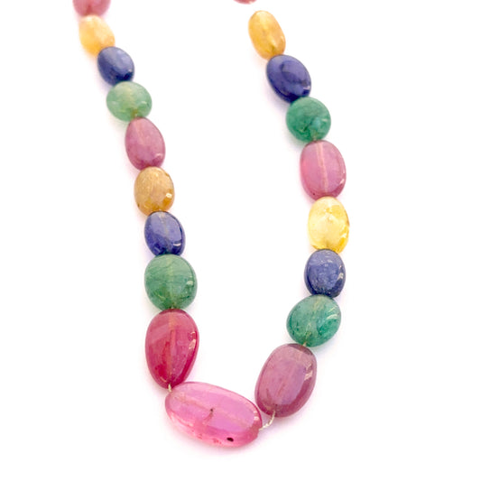 Close‑up of mixed yellow sapphire, blue sapphire, ruby and emerald smooth oval beads showing polished surfaces and vivid gemstone colour.
