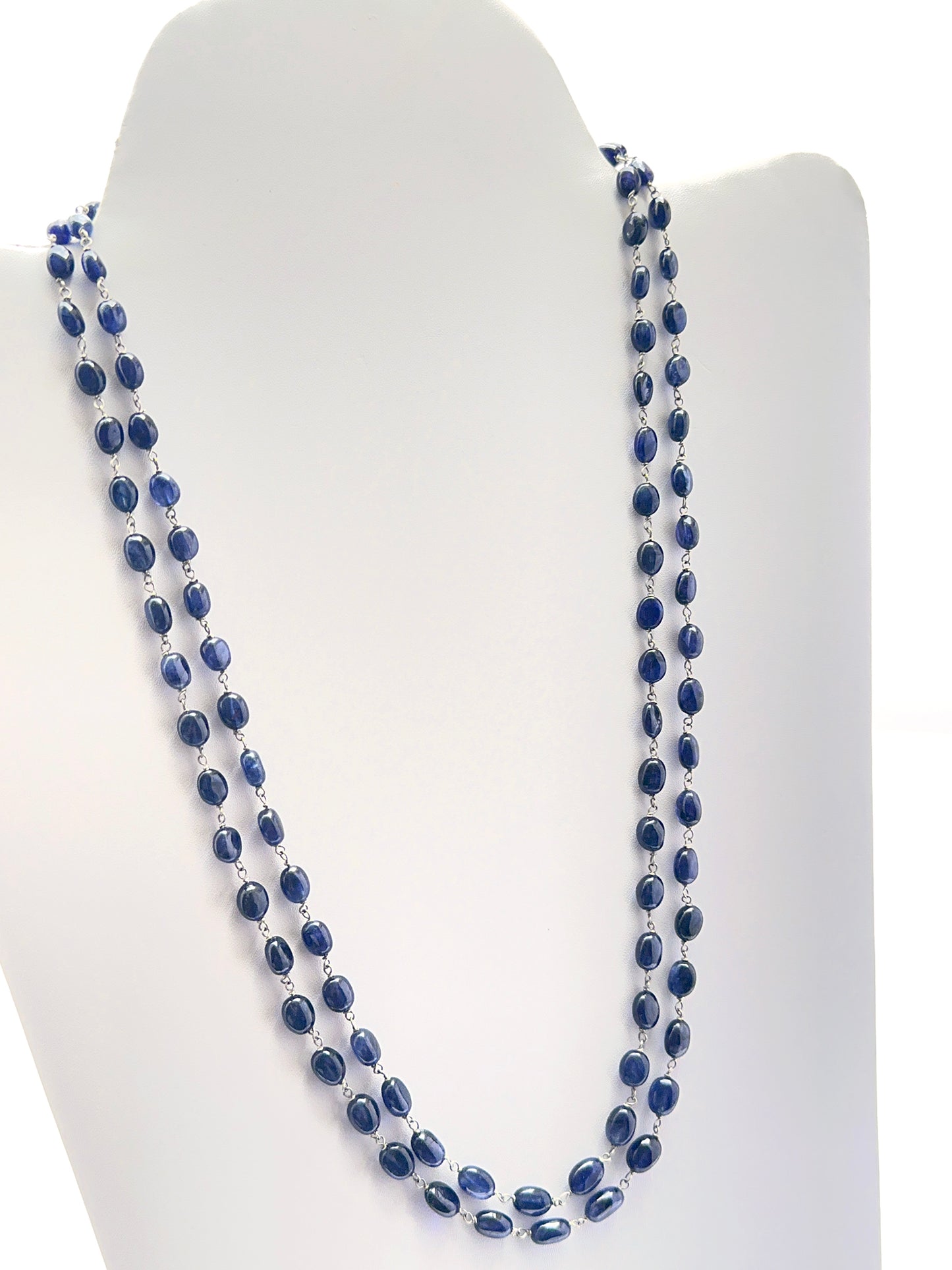 Close‑up of smooth oval sapphire beads arranged on a polished two‑strand necklace.