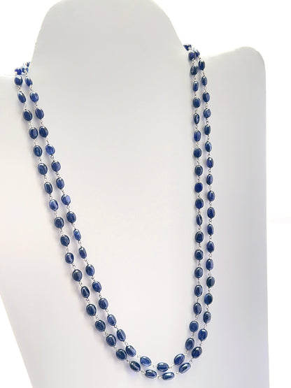 Close‑up of smooth oval sapphire beads arranged on a polished two‑strand necklace.