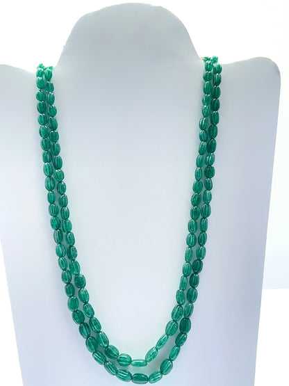 Close‑up of carved emerald beads arranged on a polished two‑strand necklace.