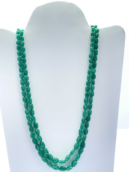 Close‑up of carved emerald beads arranged on a polished two‑strand necklace.