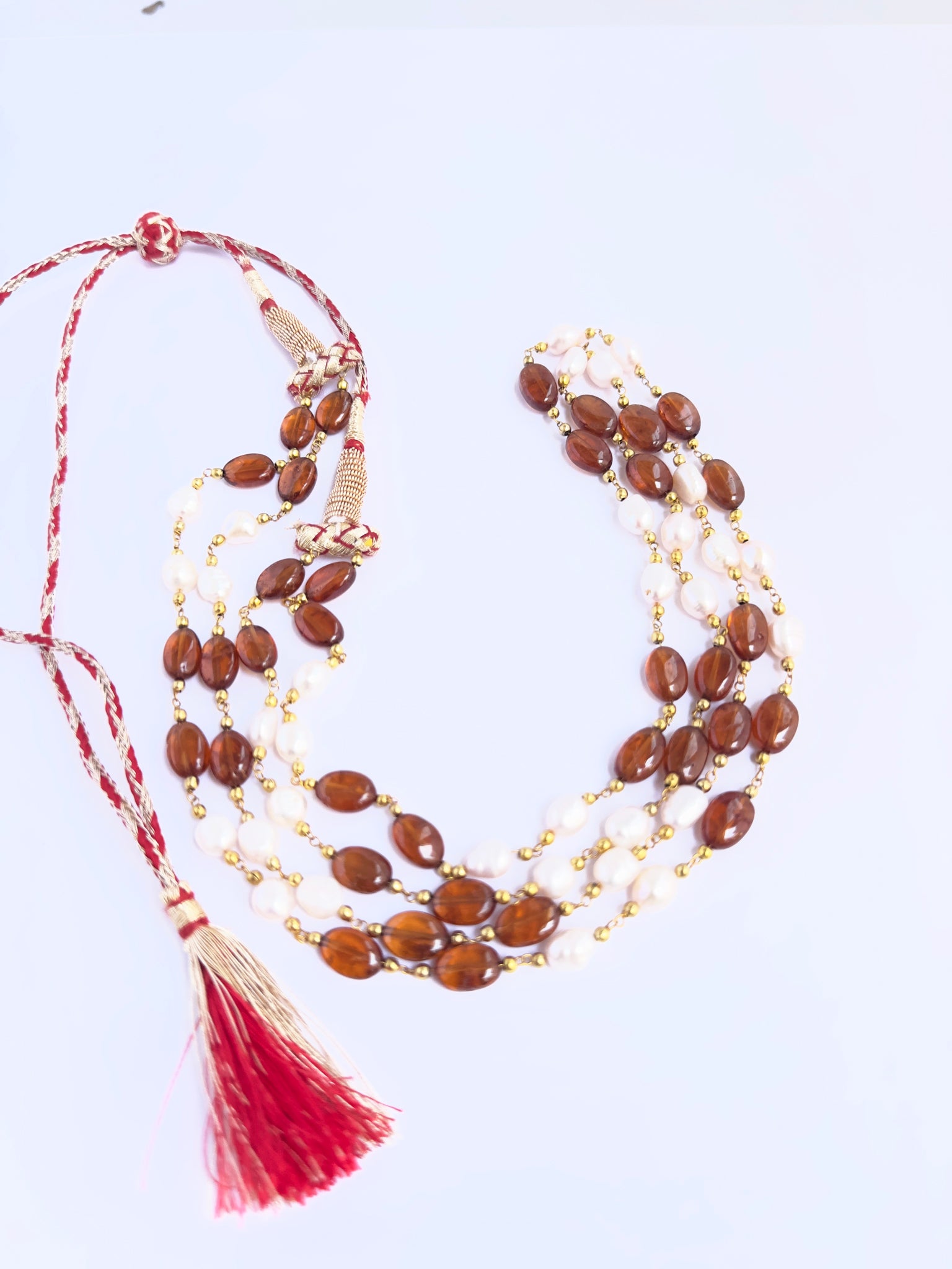 Close-up of Hessonite and pearl gemstone beads, smooth oval cut, polished finish, arranged in strands.