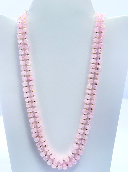 Close‑up of carved rose quartz beads arranged on a polished two‑strand necklace.